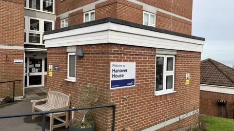 The exterior of a brick multi-storey apartment block with a sign reading 'Hanover House.'