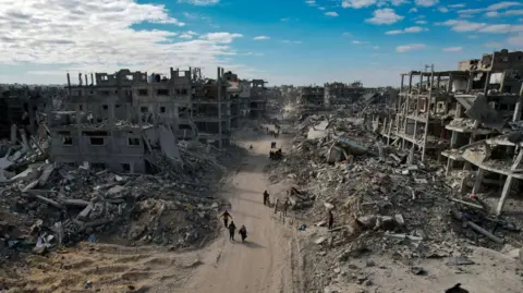 EPA Aerial photo taken with a drone shows internally displaced Palestinians walking along a street among the gray and dusty ruins of destroyed buildings in Rafah. 