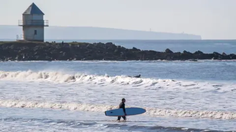 Getty Images A surfer walking into the sea at Porthcawl on a sunny day