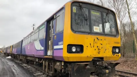 The Dales School A Pacer train which has yellow frontage and is painted purple and blue on the side. It is a Northern train.