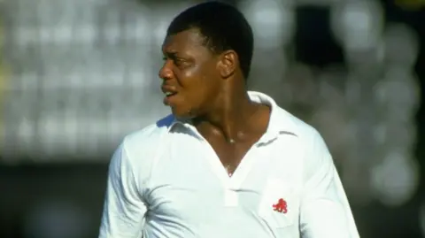 Getty Images David "Syd" Lawrence. He has short dark hair and is wearing white cricket gear. He is looking to the side.
