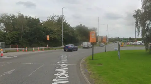 Google Maps street view of the Wick Wick Roundabout on the A4174. Traffic lights have been covered with orange material. There are orange traffic cones on and around the roundabout. There are cars exiting the roundabout.
