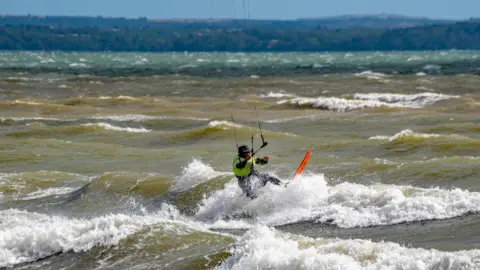 out to grass A kiteboarder rides the waves.