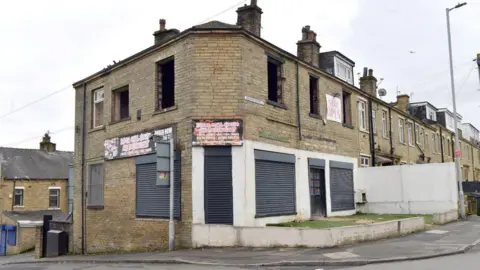 LDRS A large building at the end of a row of terraced houses. The upper floors have blow- out windows and there is some faded signage.