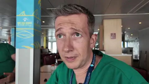 A man in medical scrubs sat looking at the camera