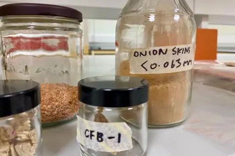 Four glass jars containing onion skins in a variety of forms with labels on the jars 