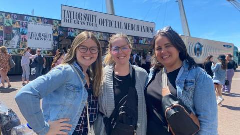 Three Taylor Swift fans pose for a group photograph outside the merchandise truck at Cardiff's Principality Stadium ahead of The Eras Tour.