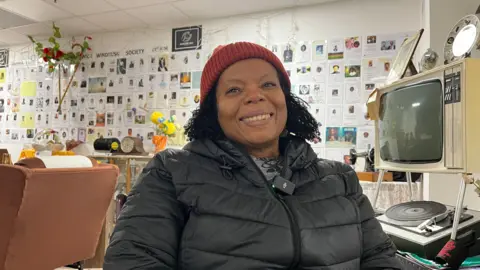 Ivy Scott wearing a black puffa jacket and a red wool hat. She is smiling and looking directly into the camera.