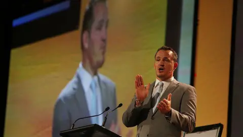 Getty Images A man in a light coloured suit stands in front of a lectern delivering a speech into a microphone. He also appears enlarged on the big screen behind him.