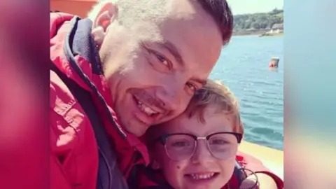 Family handout Selfie of Dean and Charlie Lowe while the father and son are on a boat. Both are smiling and wearing red coats.