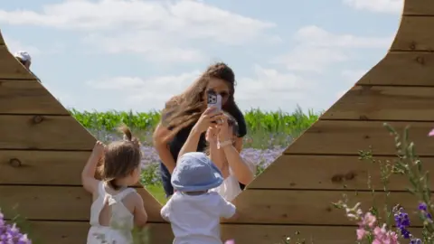 Woman taking photo of children through a wooden heart shape in flower fields