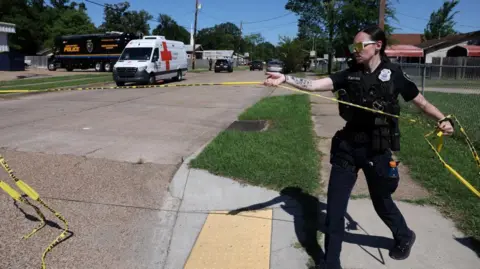 Reuters A police officer holds a police tape in a street with a police van in the distance with other vehicles, at the scene after children were killed in a mass shooting incident in Shreveport, Louisiana
