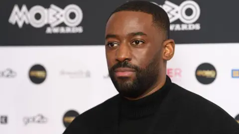 Getty Images Bashy at the Mobo Awards. He wears a black turtleneck and has a serious expression. 