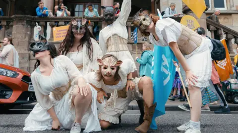Adrienne Photography A group of women wearing corsets and white dresses wearing animal masks outside Winchester Guildhall.