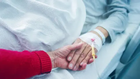 A hand holding the hand of a person lying in a hospital bed. 