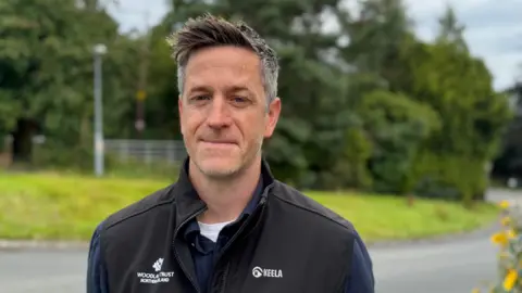 A man with spiky brown greying hair - he wears a black 