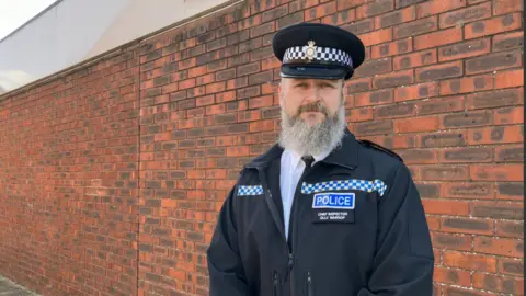 Shariqua Ahmed/BBC Ch Insp Ollie Warsop in a black police jacket and cap 