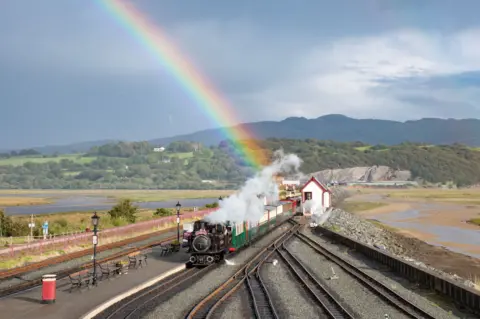 Chris Parry A steam train arrives at a station under a rainbow