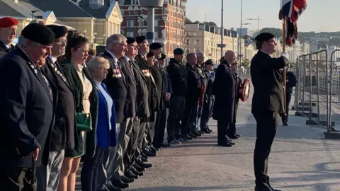 Men and women wearing medals standing to attention behind a flag bearer