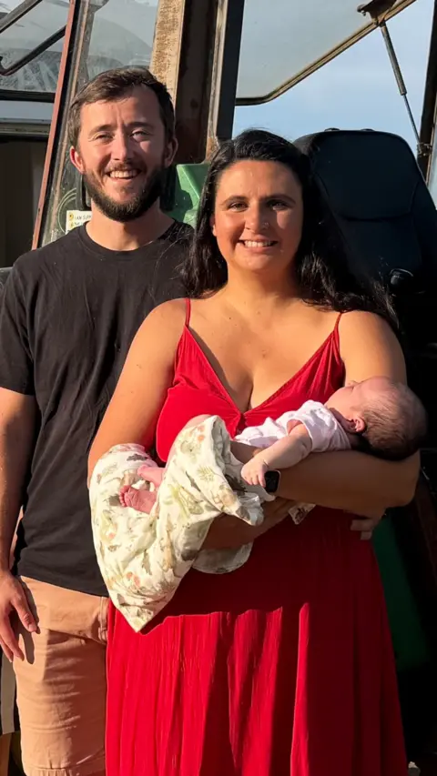 A man wearing a black t-shirt and a woman in a red dress holding a baby