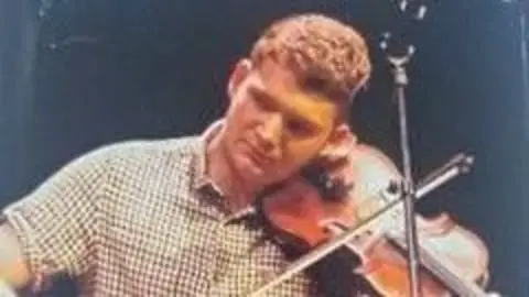 A man in a checked shirt plays the fiddle