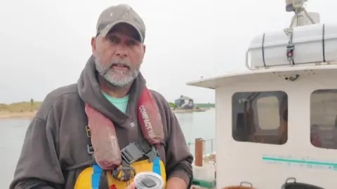 Peter on the deck of his fishing boat wearing a cap and lifejacket. 