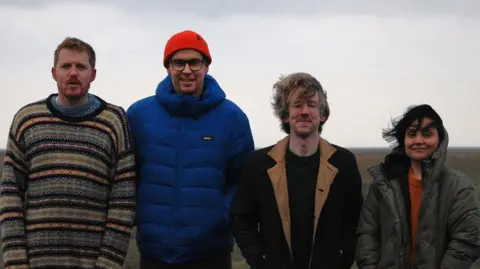Lancaster Music Co-op Four piece band Dog Daisies comprised of three men and a woman (far right) dressed in jumpers and winter coats.