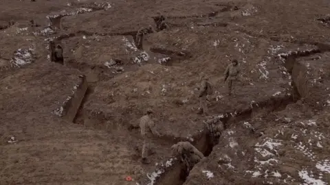 Troops wearing camouflage army uniforms clearing snow-covered trench lines