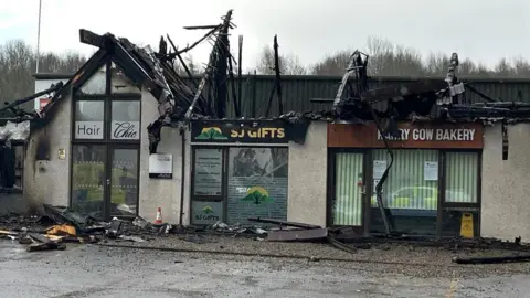 The retail units have lost their roofs and there is debris on the ground.