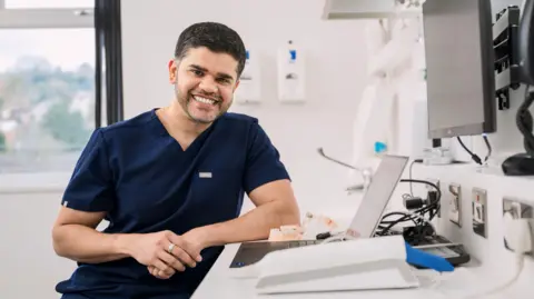 Parmar Dental Dr Nilesh Parmar leaning on a desk
