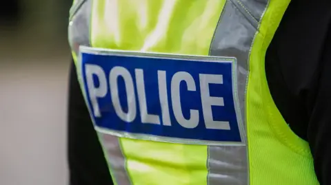 A police logo on a high-visibility jacket is seen up close. 