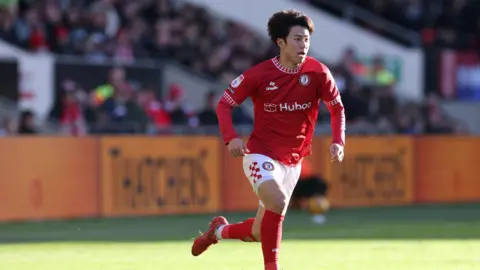 Yu Hirakawa in a red and white Bristol City kit, running across the pitch with wind in his hair.