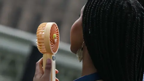 A woman with braids holds an orange hand-held fan