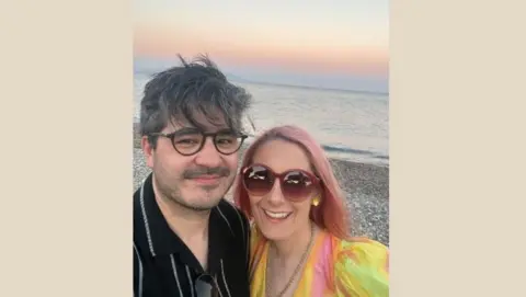 Becky Excell Mark in a black shirt and Becky with pink hair in a colourful dress, on the beach