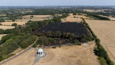 An aerial shot of a large patch of a burned field after a large grassfire caused damage. A number of other fields are in the surrounding area.