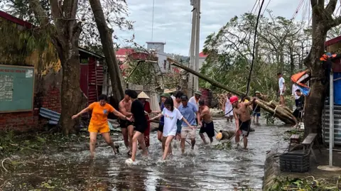 Reuters More than a dozen people wade through flood waters and use ropes to remove fallen trees following the impact of Typhoon Yagi in Hai Phong in northern Vietnam