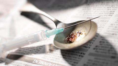Needle and spoon with heroin resting on a newspaper