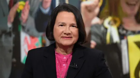 BBC Catherine West sitting in a studio looking directly at the camera, wearing a black blazer and a pink shirt.