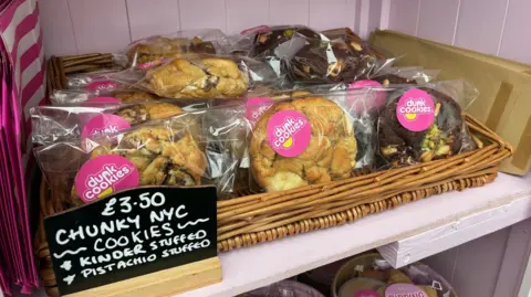 Tray of cookies in the Blean Bakery Box with a sign that reads: "£3.50 chunky NYC cookies; Kinder stuffed; Pistachio stuffed".