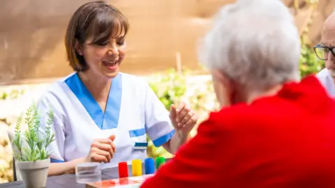 Getty Images A carer wearing a uniform playing a board game that has brightly-coloured counters with an elderly person with white hair, wearing a red top.