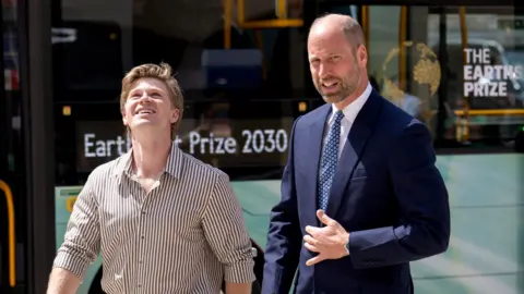 Prince William gets off a tourquise coloured bus wearing a suit and tie