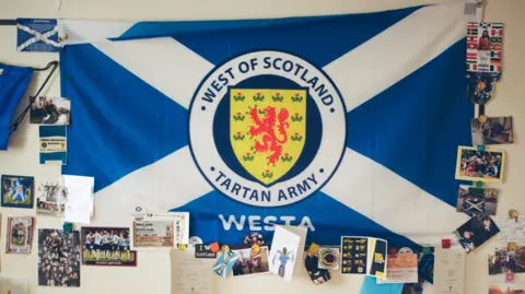 Craig Mcintosh Scotland Tartan Army supporter flag handing on the wall with football themed postcards and pictures pinned around it. 