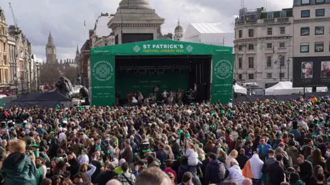 PA Media An image showing crowds of people looking towards a stage in Trafalgar Square covered in green tarpaulin saying 'St Patrick's Festival London 2024'