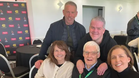 A group photograph of Frank Wignall smiling, flanked by his daughters Caroline O'Loughlin and Lynne Abbott. Behind them is on in law Graham Abbott and Frank's  son Stephen Wignall. They are at a dementia support group Forget Me Notts at Nottinghamshire Cricket Club