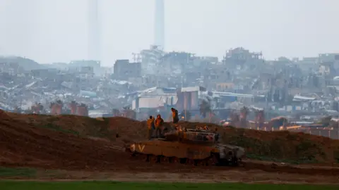 Reuters Israeli soldiers stand on top of a tank in southern Israel, near the frontier with Gaza (12 February 2025)