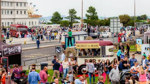 Vintage By The Sea Crowds milling round stalls in Morecambe with Morecambe Bay in the distance