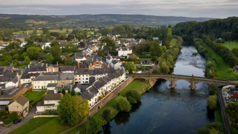 Getty Images Aerial view of Usk and the river Usk with old stone bridge with arches over the river, houses to the left and green fields and mountains beyond