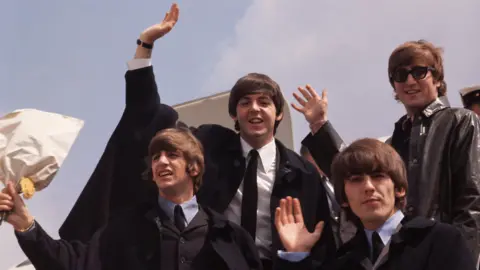 The Beatles wave as they step off an airplane in 1964