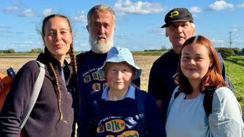 Mike Liggins Cecile Roberts (left) wearing a black fleece and is carrying an orange back pack. She is stood with two men and two women who are taking part in the charity walk. 