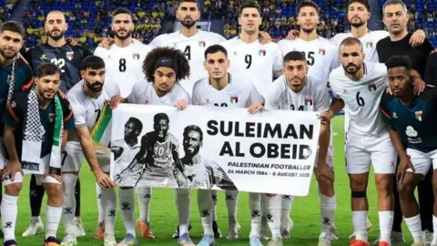 Palestinian Football Association Players on a football pitch hold a poster with Obeidi's picture in tribute